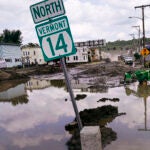 A small tractor clears water from a business as flood waters block a street in Barre, Vt.