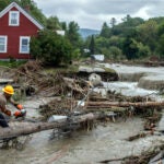 Zac Drown, of Lyndon Electric Company, clears debris amid flood damage in Lyndon, Vt.